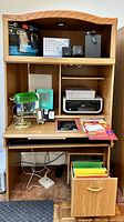 Full view of the multi-purpose wood shelving and desk unit showing various accessories and electronics placed on shelves and desktop, including lamp, folders, printer, and supplies.