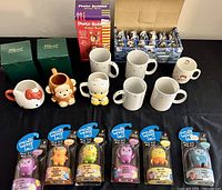 Overview photo showing novelty mugs (including Hello Kitty and monkey), Whippoorwill American Artisans mugs, and 6 packaged Moji-Mis figurines.