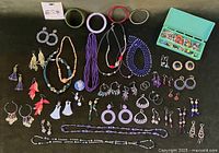Overview of the assortment showing multiple pairs of earrings, several necklaces, and a turquoise box containing jewelry findings.