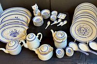 Blue and white porcelain collection arranged with plates, various bowls, teapots, serving spoons, and a cat creamer.