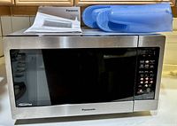 Full front view of Panasonic inverter microwave oven with control panel, silicone oven mitts on top and owner's manual.