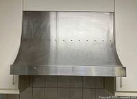 Front view of curved stainless steel range hood mounted between kitchen cabinets above stove area.