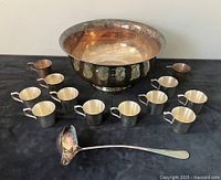 Full set including punch bowl, 12 cups, and ladle arranged on a dark surface, highlighting reflective tarnished silver plated surfaces.