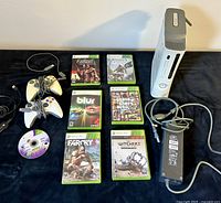 Xbox 360 console, two controllers, six game cases, power adapter, and AV cable laid out on a black surface.