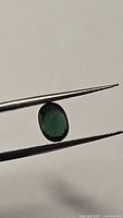 Close-up photo of an oval cut green-blue tourmaline gemstone held by tweezers showing its color and clarity.