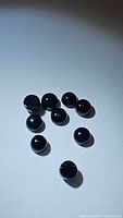 Ten small, round, polished black cabochon onyx stones arranged loosely on a white surface with soft lighting showing glossy domed tops and flat backs.