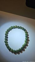 Natural green jade bracelet laid flat, showing round polished beads with a glossy finish under spotlight.