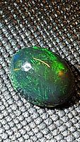 Close-up showing oval cut black opal with bright green flashes on a textured background.