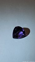 Close-up photo of single deep purple pear-shaped amethyst gemstone with facets visible showing reflections and clarity.