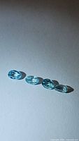 Four natural blue oval zircon gemstones arranged on a white surface, showing their blue color and facets under lighting.
