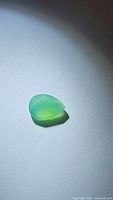 Photo of natural vivid green onyx gemstone with pear shape and checkerboard cut under light showing translucency and facet details.