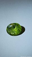 Oval cut natural peridot gemstone in apple green color showing internal inclusions