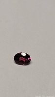 Close-up photo of oval cut hot pink purple garnet gemstone on a neutral background with light reflection.