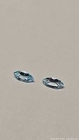 Two marquis cut sky blue topaz gemstones lying flat on a neutral background to show color and cut.