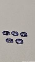 Five oval cut tanzanite gemstones arranged on a neutral background, showing size and color.