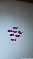 Seven marquis cut red-pink natural untreated ruby gemstones on a white background, showing color and clarity.