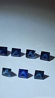 Photo showing seven princess cut blue sapphires arranged with lighting highlighting their facets and deep blue color.