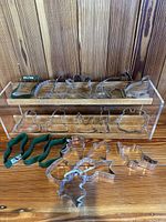 Display of 20 metal cookie cutters arranged on clear acrylic stand and table, showing various shapes including animals, people, and seasonal motifs.