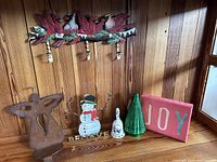 Photo of six Christmas decorative items including cardinal bird wall hooks, metal angel figure, wooden snowman, ceramic bell, green tree, and JOY block sign.