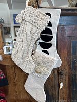 3 Christmas stockings hanging on wooden surface showing cream knitted cable knit, cream textured felt, and modern cream stocking with red and olive circles