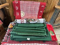 Stack of folded items including red cloth with numbers, woven cloth with holiday embroidery, green cloth coverings
