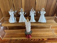 Set of four clear plastic angel ornaments posing with one candle-shaped ornament with greenery and red base. All items have hangers or switches visible.