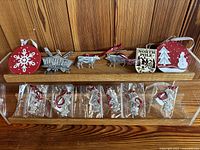 Overall set of Christmas ornaments on wooden display including wood and metal figures and packaged metal pieces.