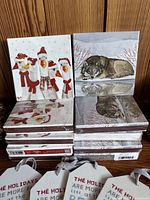 Stacks of 10 matchbooks with snowmen and wolf holiday illustrations, and several dozen gift tags printed with holiday messages tied with ribbons