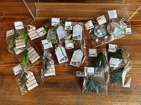 Photo showing multiple holiday decorative gift tags in individual clear plastic packaging on wooden surface, including tags with "happy holidays" and "enjoy" messages and various artificial greenery sprigs attached.