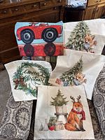 Lot of five new decorative pillow covers with Christmas themes including animals, trees, gifts, and holiday greetings, arranged on a patterned cushion.