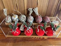 Full view of the set of 10 fabric decorative ornaments arranged in two rows on a wooden surface, showing five patterned fabric balls with tassels and five red fabric balls decorated with pine springs and pinecones.