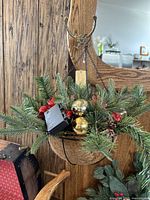 Hanging basket with artificial evergreen branches, gold baubles, and red berry decorations on wooden background.