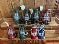 Front view of 8 Christmas themed decorative lanterns showing various sizes and colors including pine cone and berry decorations.