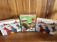 Set of three sealed jigsaw puzzle boxes with winter scenes and festive decoration, placed against wooden wall.