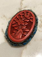 Front view showing oval cinnabar floral design, braided border and blue cloisonné accents.