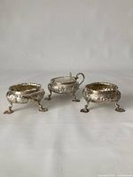 Three silver pieces—mustard pot at center, salt cellars on either side—front view
