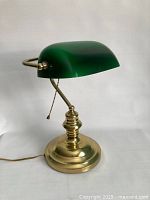 Front and full view of the banker’s desk lamp showing the green glass shade and polished brass base with pull chain.