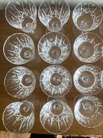Top-down view of twelve vintage cut crystal glasses arranged in three rows showcasing detailed geometric star and diamond cut patterns on the bowl and stem of each glass.