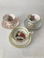 Three Royal Stafford teacups and saucers in pastel colors with floral patterns and gold trim on a white background.