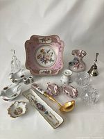 Full lot arranged on white cloth, showing all porcelain and crystal items including dessert bowl, trinket dishes, swan salt cellars, vase, candle holders, relish tray, candlestick holders, dinner bells, and various small decorative pieces.