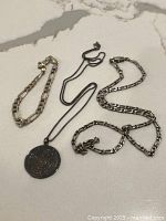 All three sterling silver jewelry items displayed together on a light marble surface: Figaro bracelet, Mexican embossed pendant on a chain, and vintage Figaro necklace.