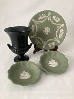 Photo showing the complete set: one black urn vase and three green Jasperware items including one large plate and two small trinket dishes
