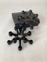 Two cast iron spider candle holders; one matte black on top of a black Dansk Designs Ltd box; the other shinier black cast iron in front