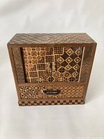 Front view of the closed jewelry box showing the patterned front doors and a single drawer below with geometric marquetry design.