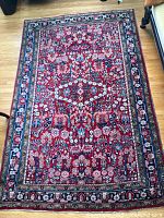 Full view of rectangular rug on hardwood floor showing red field with floral border
