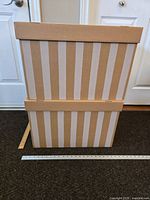 Two beige cardboard storage boxes with vertical white stripes stacked with lids. A measuring tape nearby shows box size.