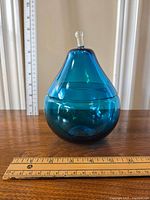 Blue pear-shaped glass compote placed on wooden surface with measuring ruler showing height around 6 inches.