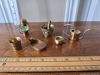 Front view of six brass miniatures on wooden table with ruler for scale, showing detailed sizes and condition.