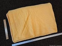 Folded large yellow wool blanket with rulers beside to show dimensions, fabric texture visible