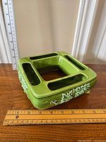 Top and angled side view of a green ceramic square planter with four narrow rectangular sections and central hollow, decorative leaf designs on sides. Includes measuring rulers for scale.